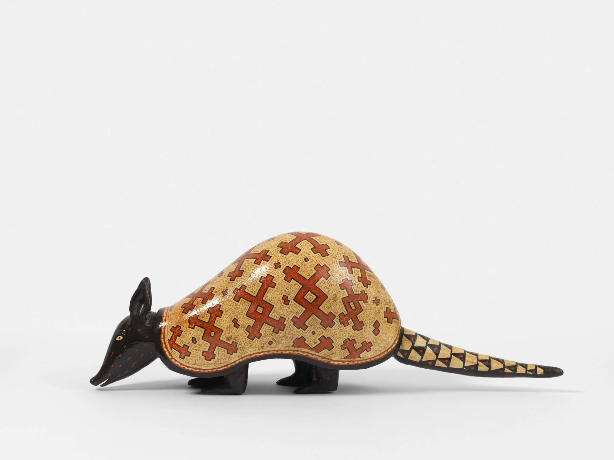 A ceramic sculpture of an armadillo with a black head, tail, and feat, and an outer shell with red and beige geometric patterns.