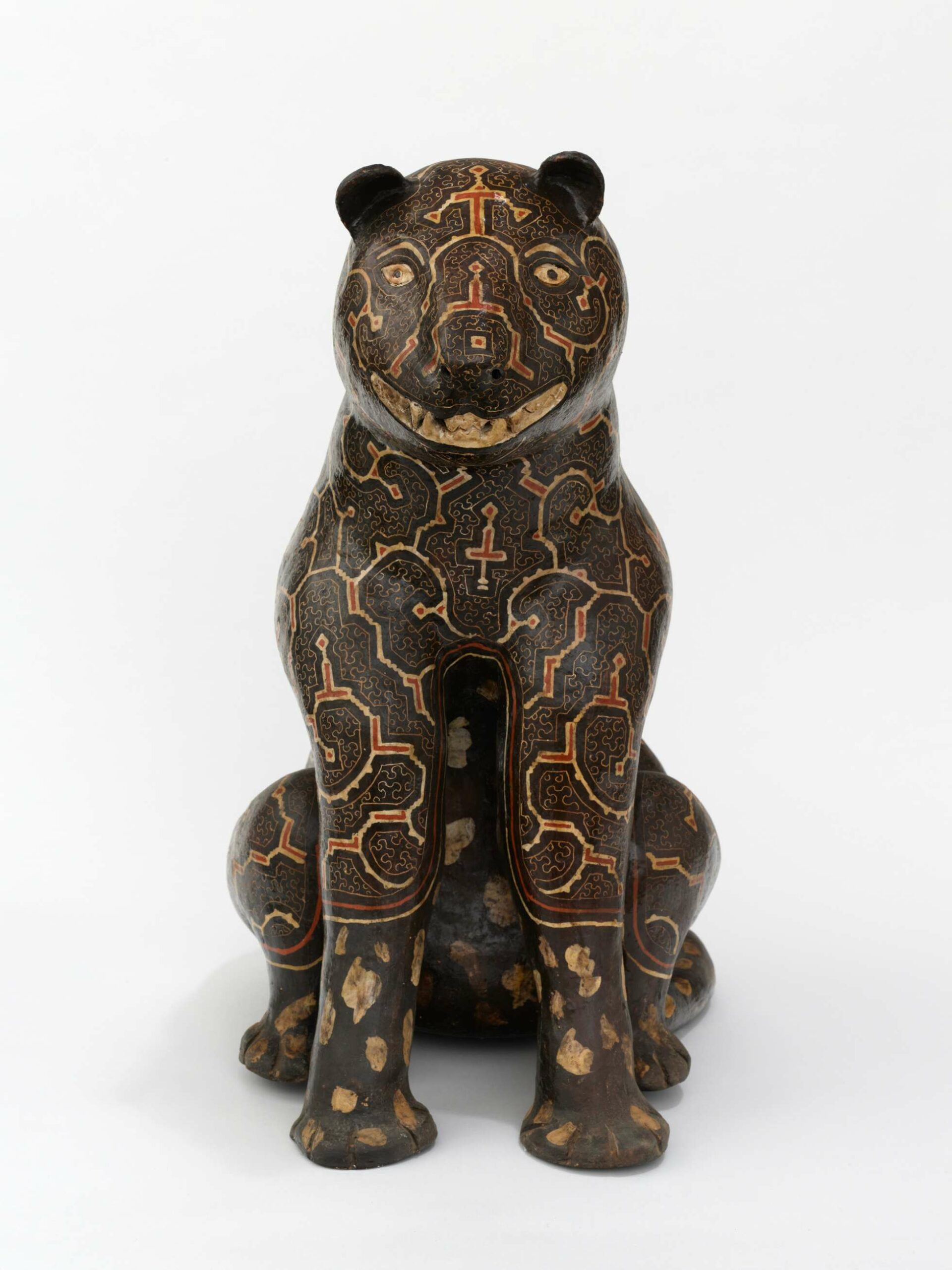 A ceramic sculpture of a black jaguar sitting on its hind legs. The body of the jaguar is etched with rounded geometric patterns in beige and terracotta red.