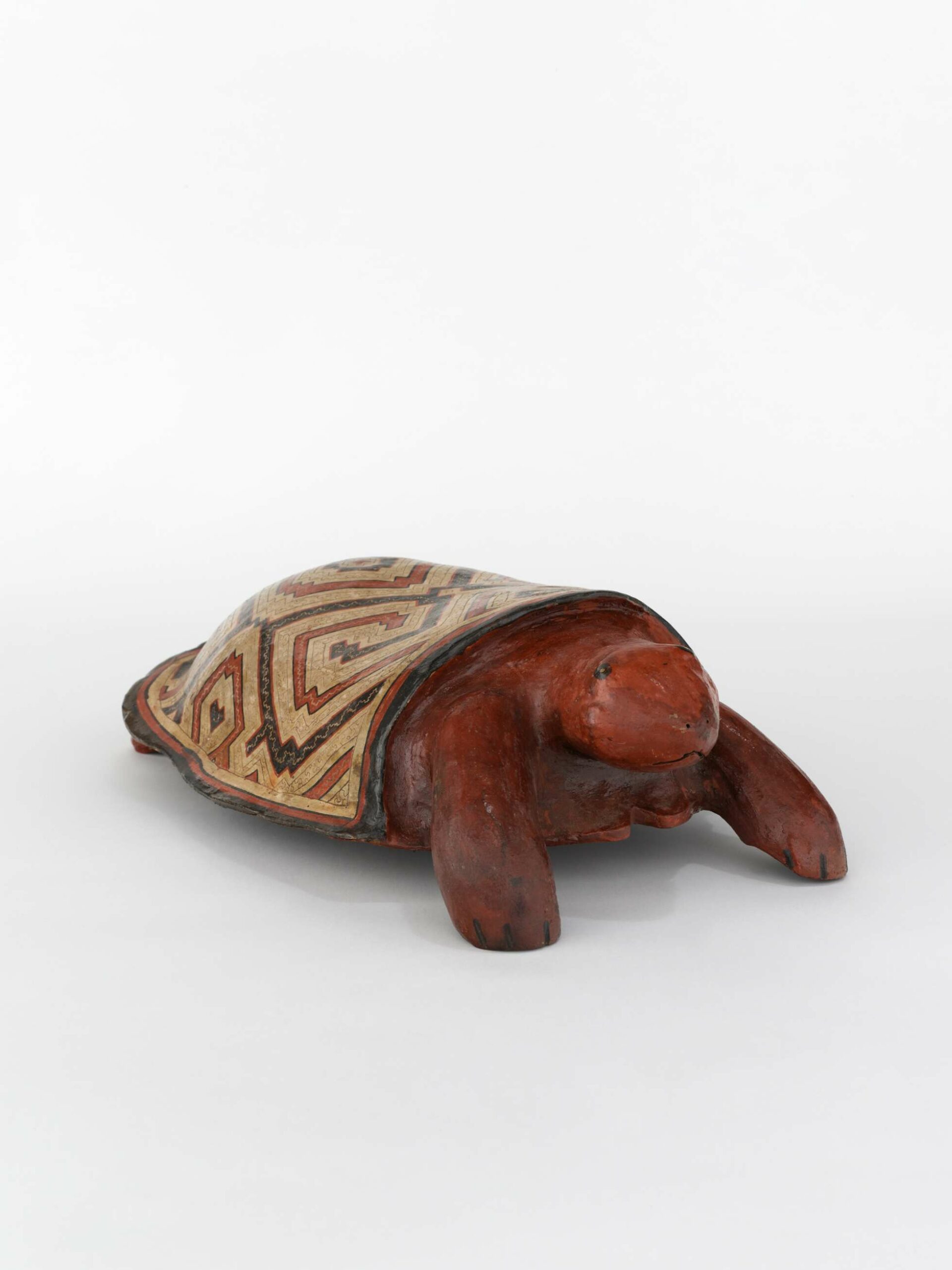 A ceramic sculpture of a turtle covered in orange-red resin. Its shell is beige colored and etched with black and terracotta geometric patterns.