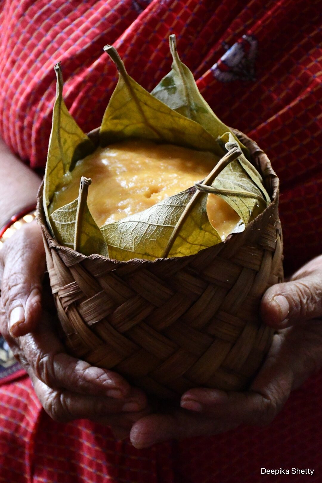 A close up shot of a single yellow jackfruit idli is steamed in leaves and held with two hands.