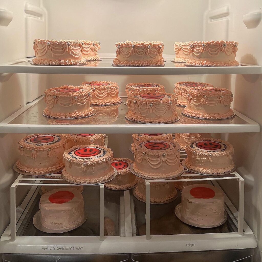 Several pink decorated cakes with smiley faces line the inside of a refrigerator