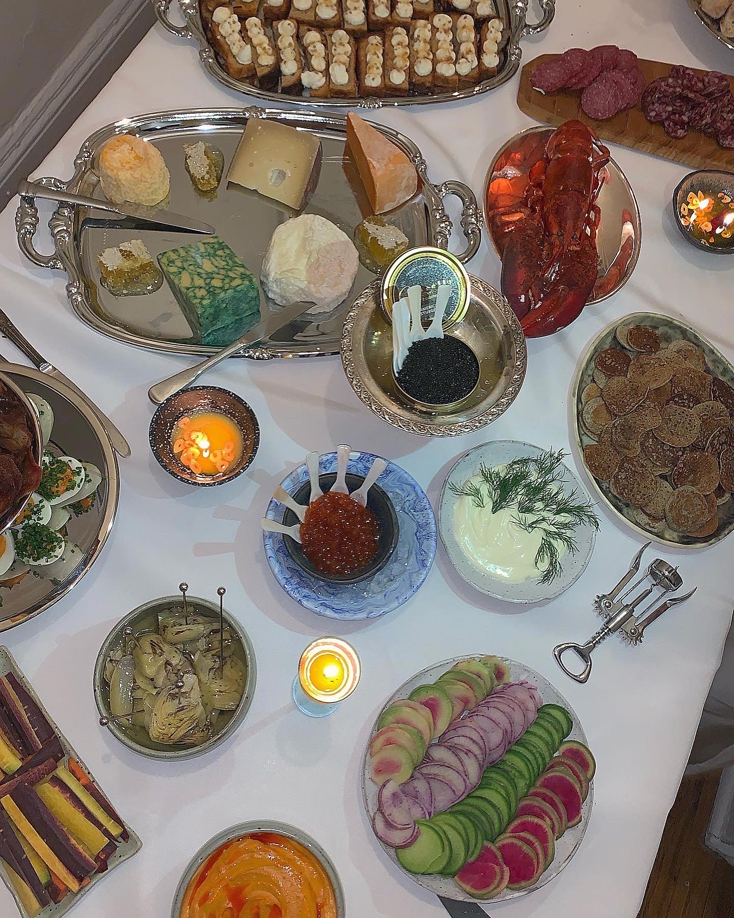 A dinner spread featuring a cheese board, plates of caviar, and crudites on platters arranged on a white tablecloth