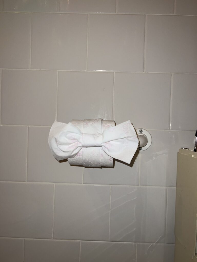 A toilet paper roll attached to the wall with hello kitty patterns on it. The toilet paper roll is fashioned in the shape of a bow.