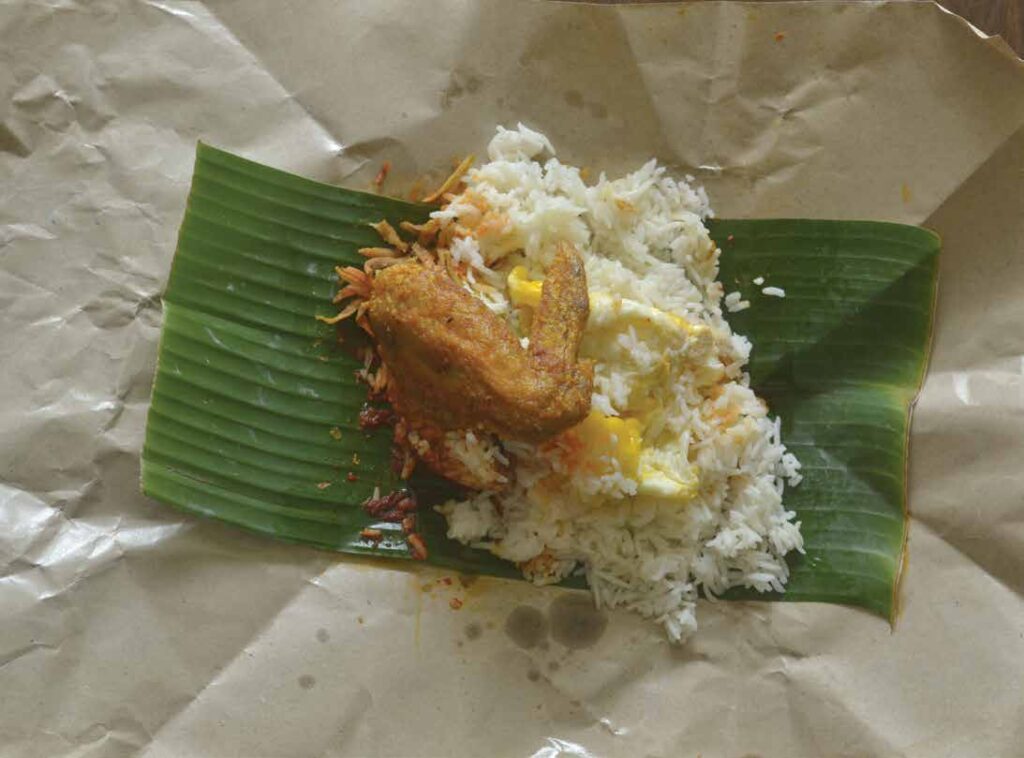 A picture of an unfolded tapow paper with a leaf and chicken and egg dish on top of it.