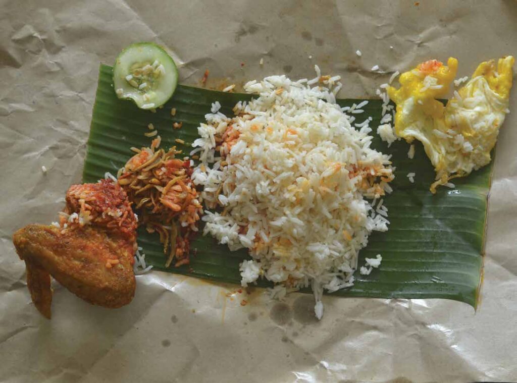A picture of an unfolded tapow paper with meal dissected on top of it. Rice, chicken and egg seperated.