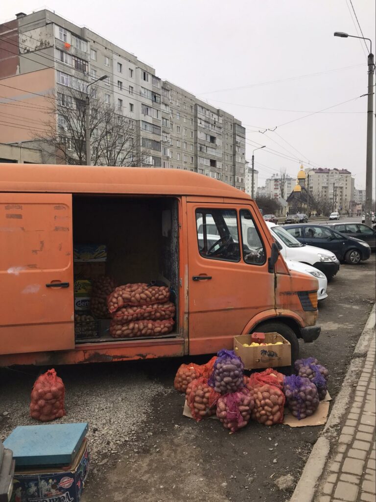 An orange truck parked alongside a street, it's door is open and there are bags of potatoes in and around the truck.