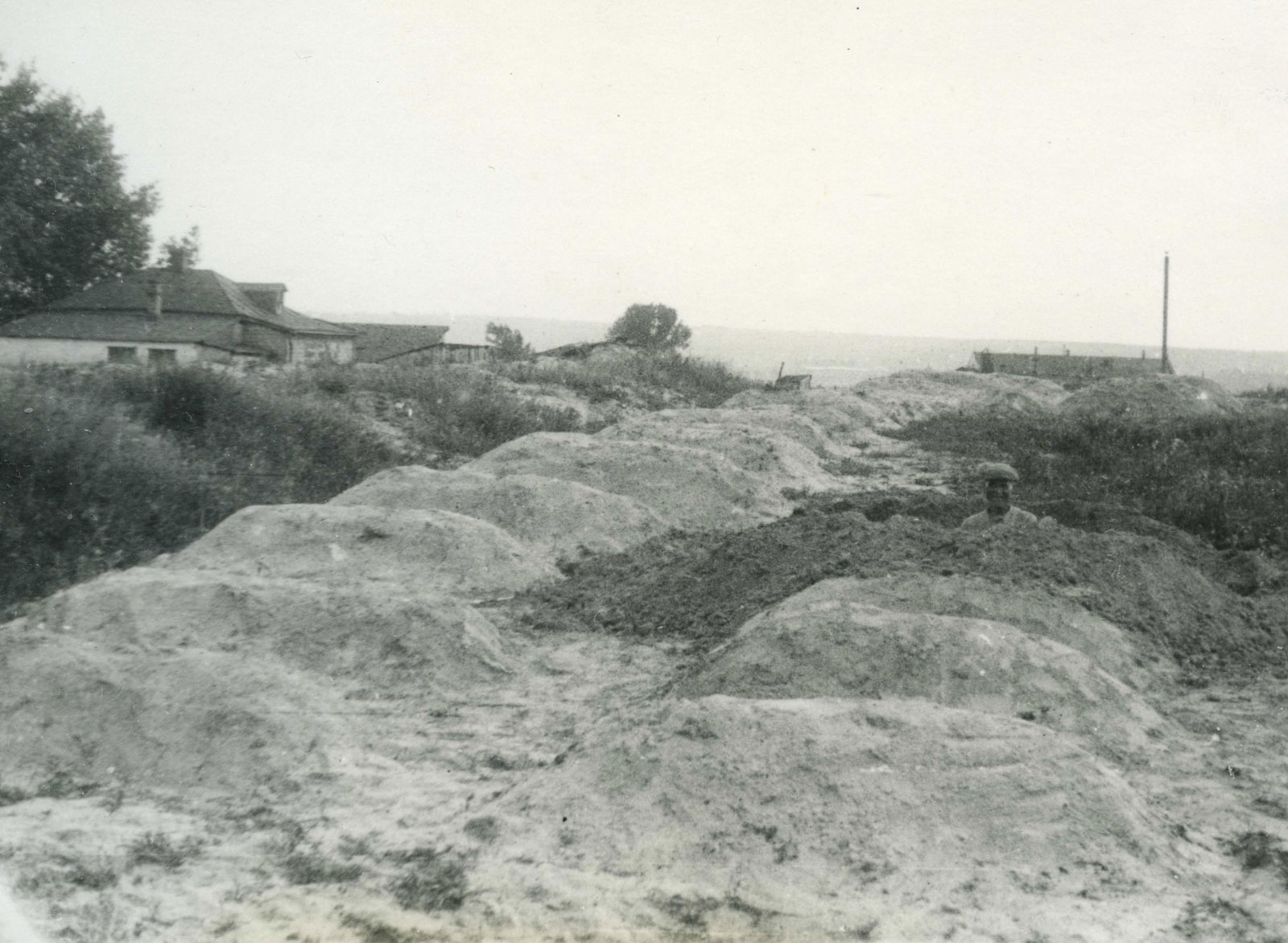 A black and white photo of several dirt mounds ordered in rows. The dirt mounds extend into the distance.