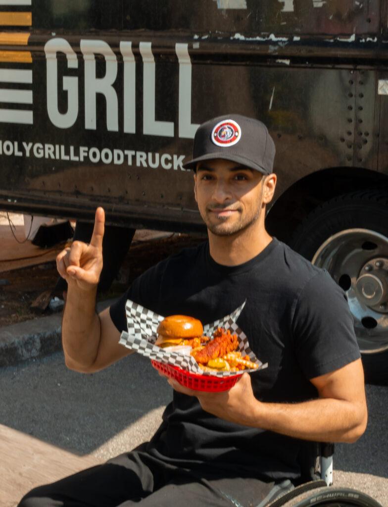 A portrait of Chef Aleem Syed holding his food outside his food truck.