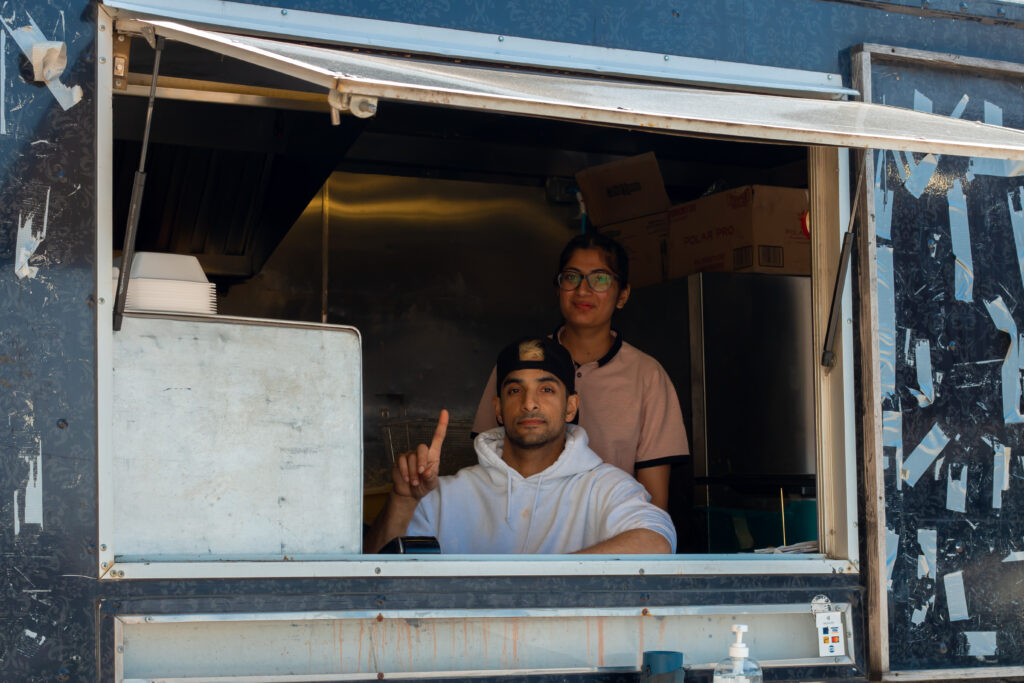 A photo of Aleem and a member of his looking out from the service window of the truck and posing.
