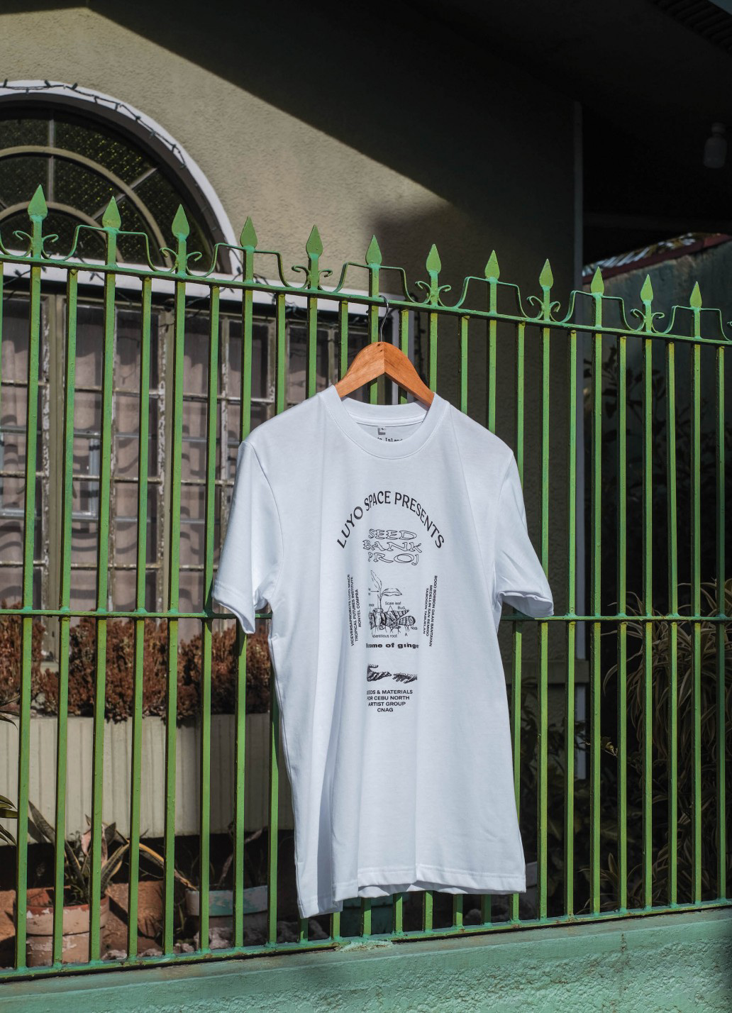 A t-shirt hangs on green metal gates that surround what looks like a residential space.
