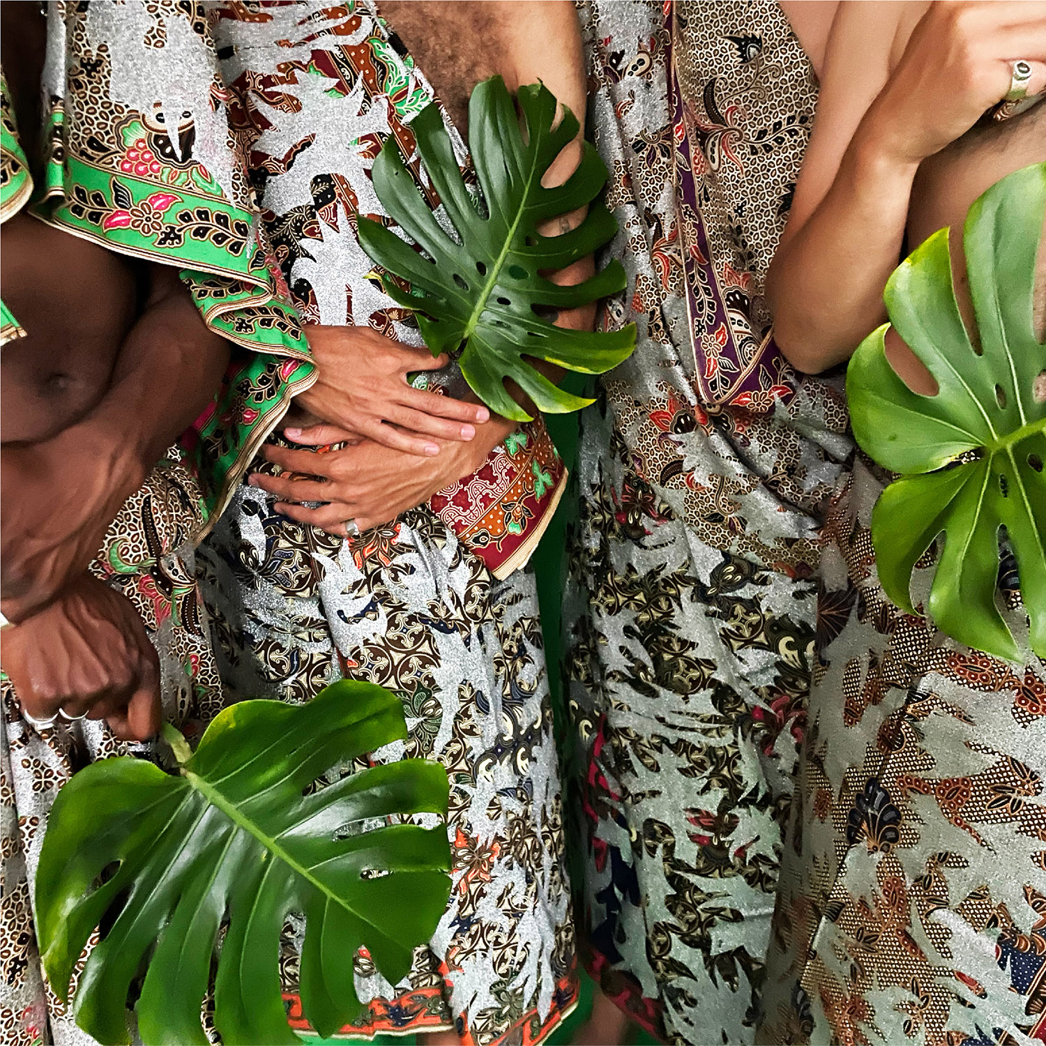 Four bodies draped in a Filipinx sarong pattern designed by Chris Fussner and Zeus Bascon of Tropical Futures Institute. Three of the people are holding large monstera leaves.