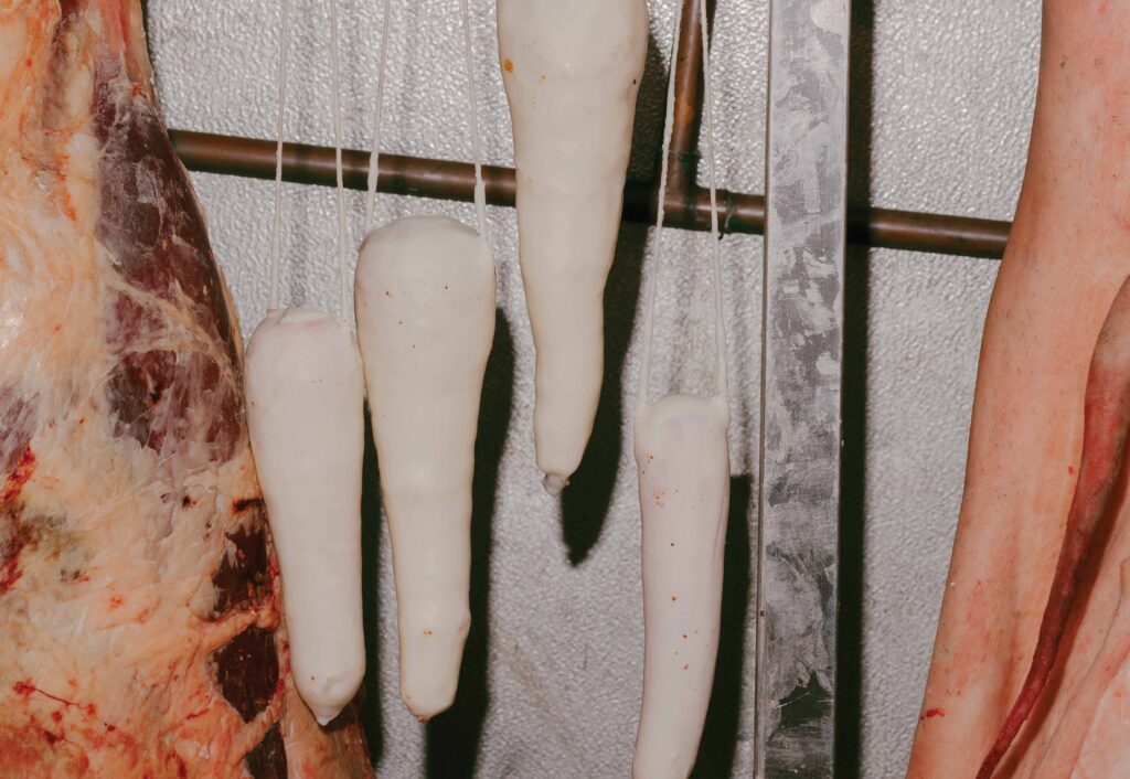 Photo of radishes hanging alongside butchered meat in a cellar.