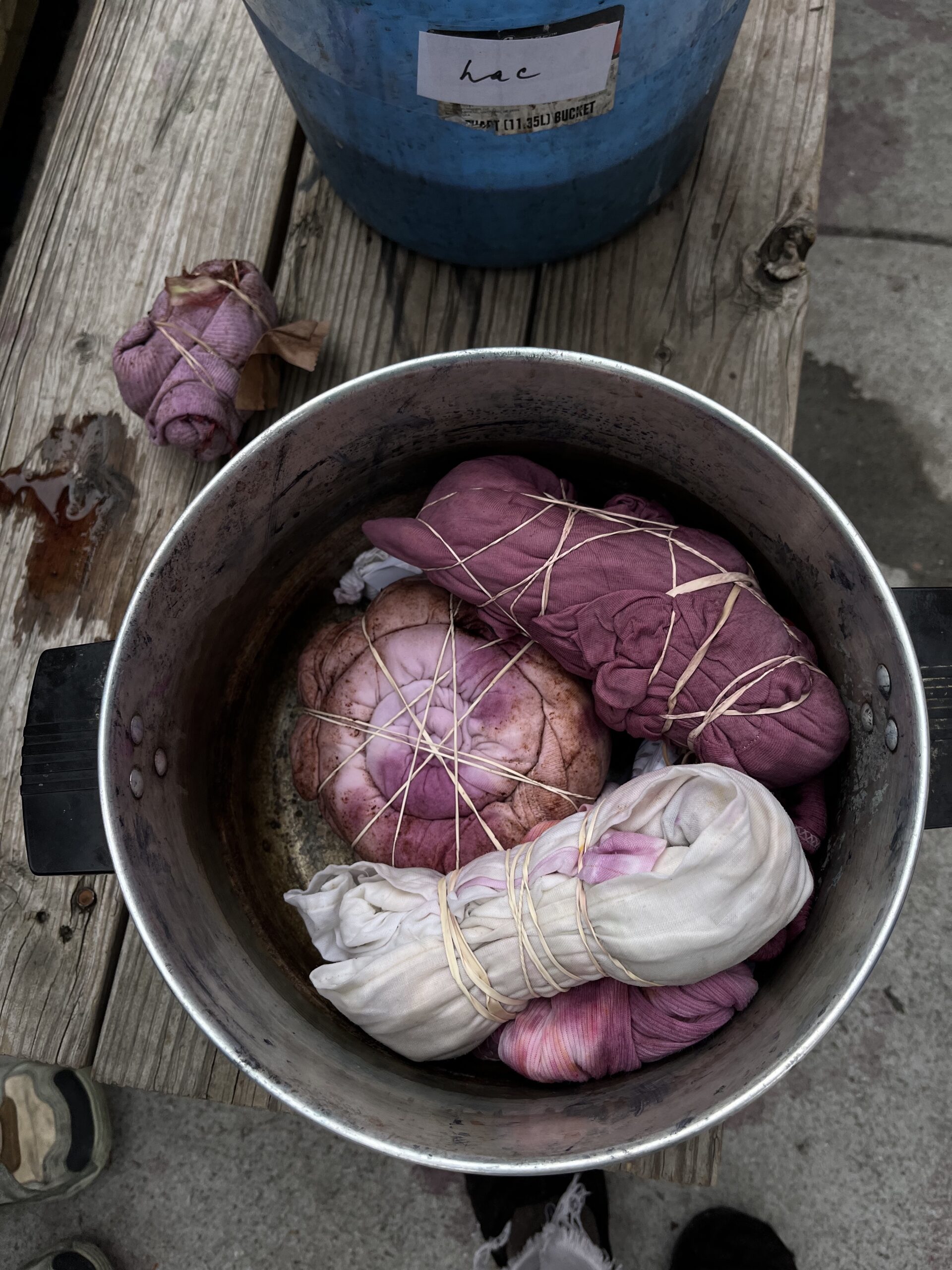 A steel pot holds three purple-dyed garments, rubber bands criss cross in preparation for tie dye.
