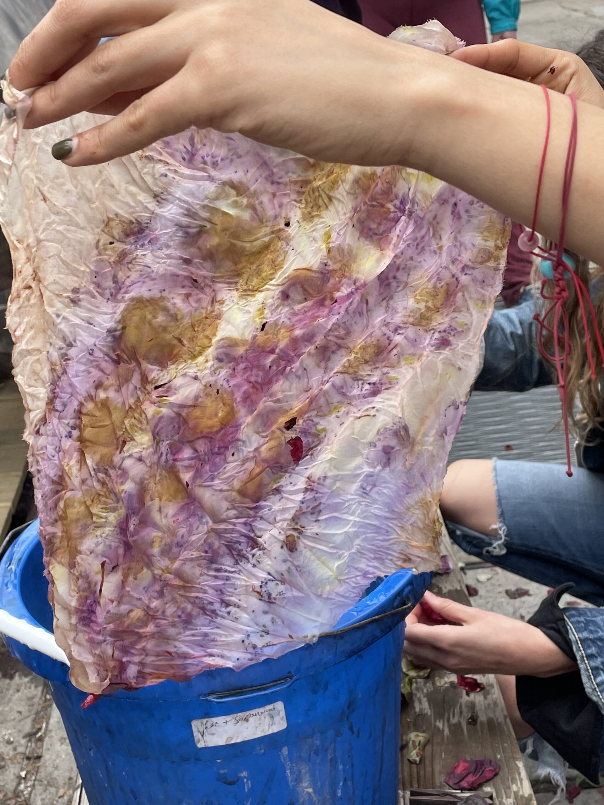 Two hands hold open a naturally dyed textile smeared with ochres and lavender coloring.
