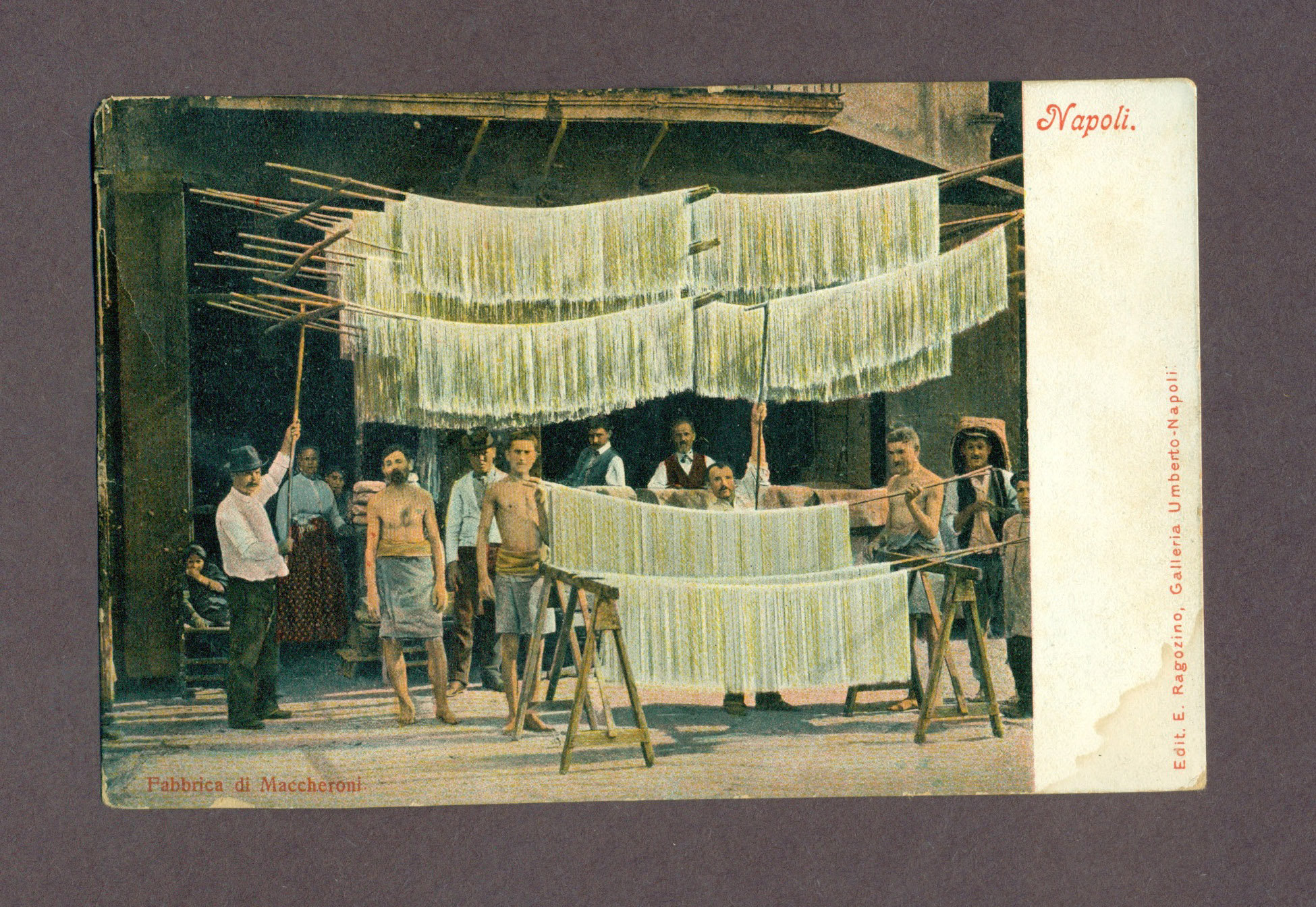 A postcard with an image of several men hanging under pasta-driers with long strands of spaghetti hanging from them. The postcard is titled Napoli.