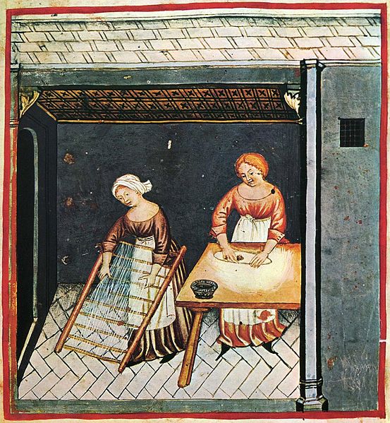 A medieval drawing of two women in a kitchen, one is rolling out dough for pasta on a table, another is nearby hanging strands of pasta to dry.