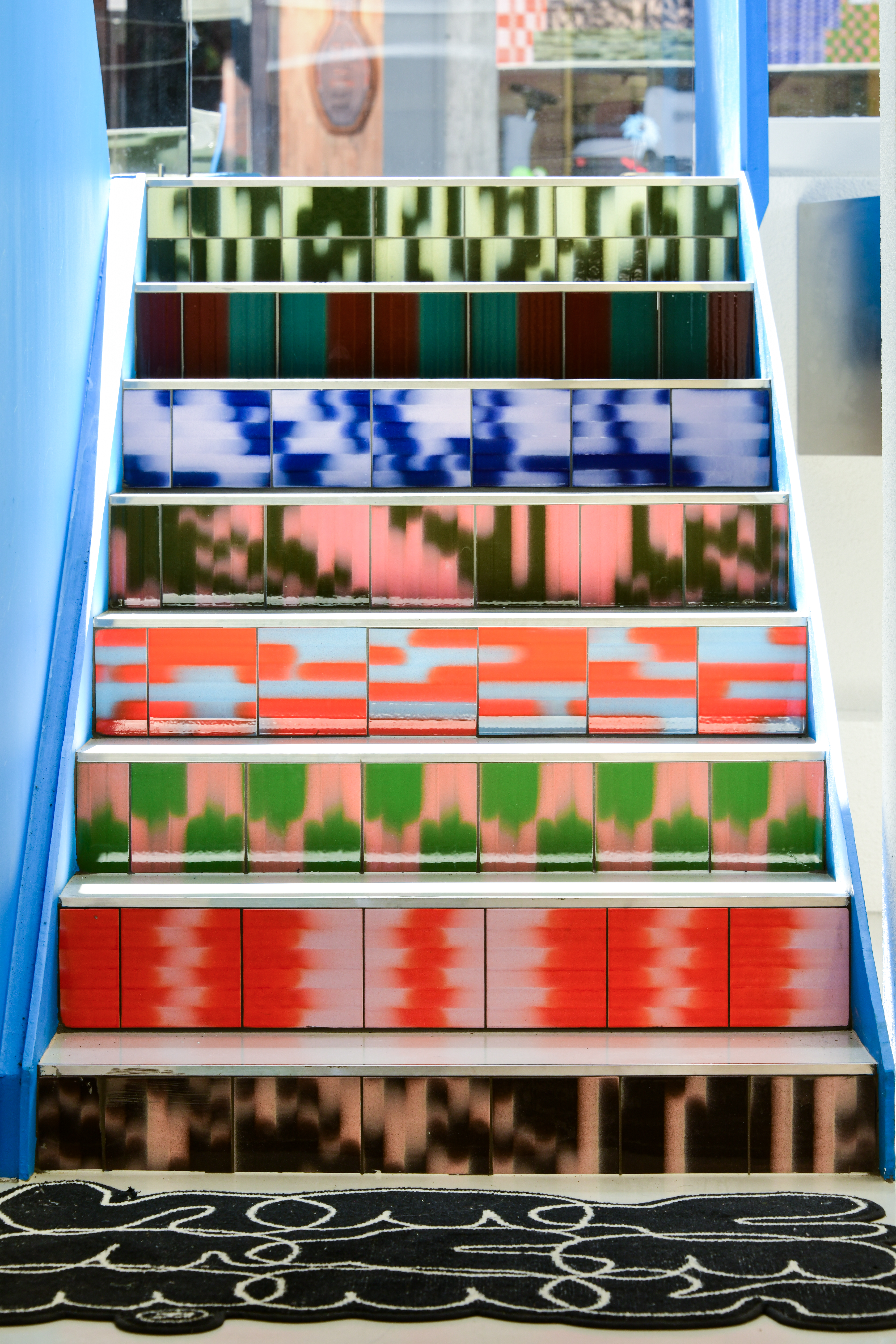 A stairway with each stair tiled with gradient tiles in various colorful patterns. 
