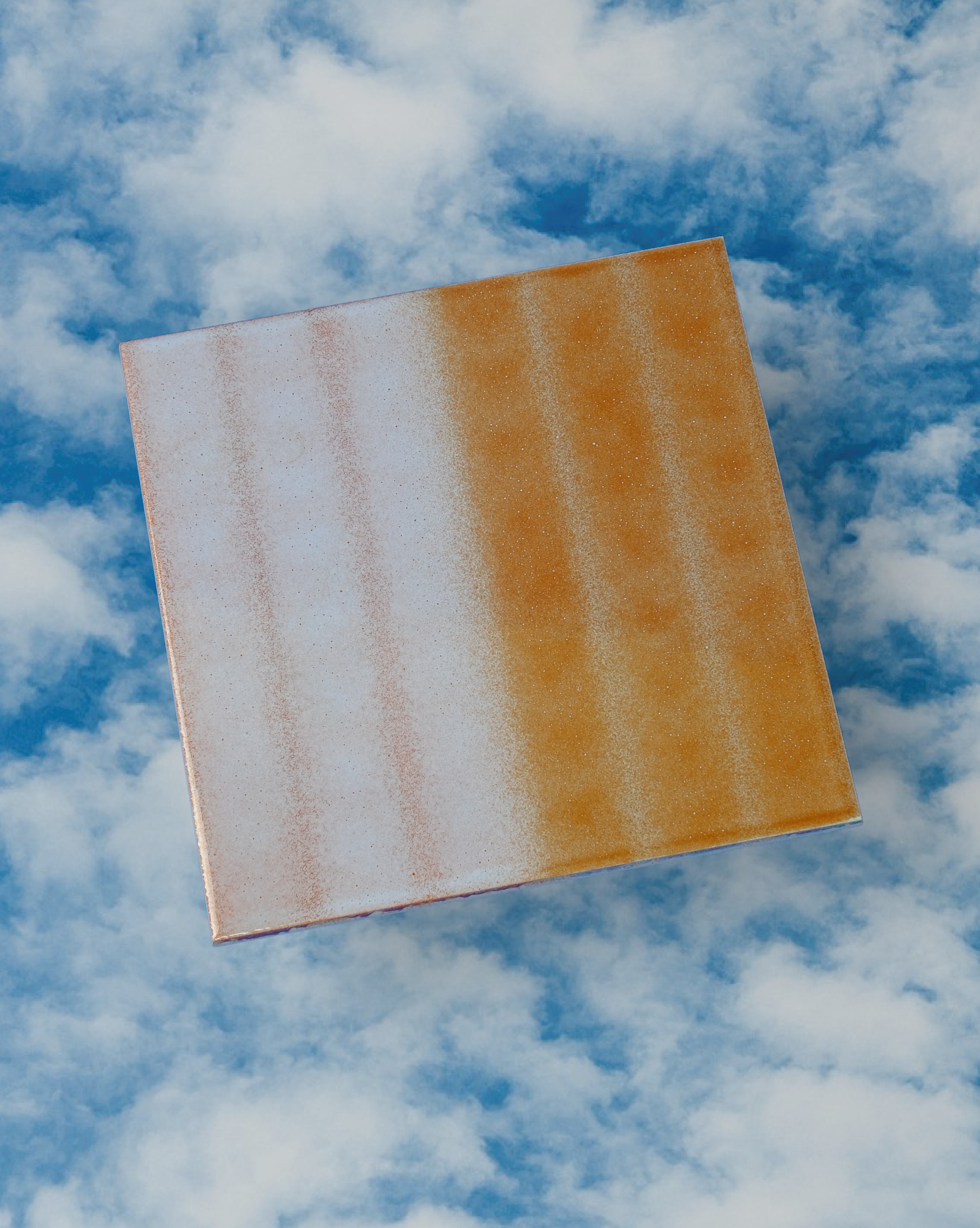 A single ceramic tile, it's glaze half pale white with thin yellow striping and the other half yellow with thin white striping is positioned against a photo background consisting of cloudy blue skies
