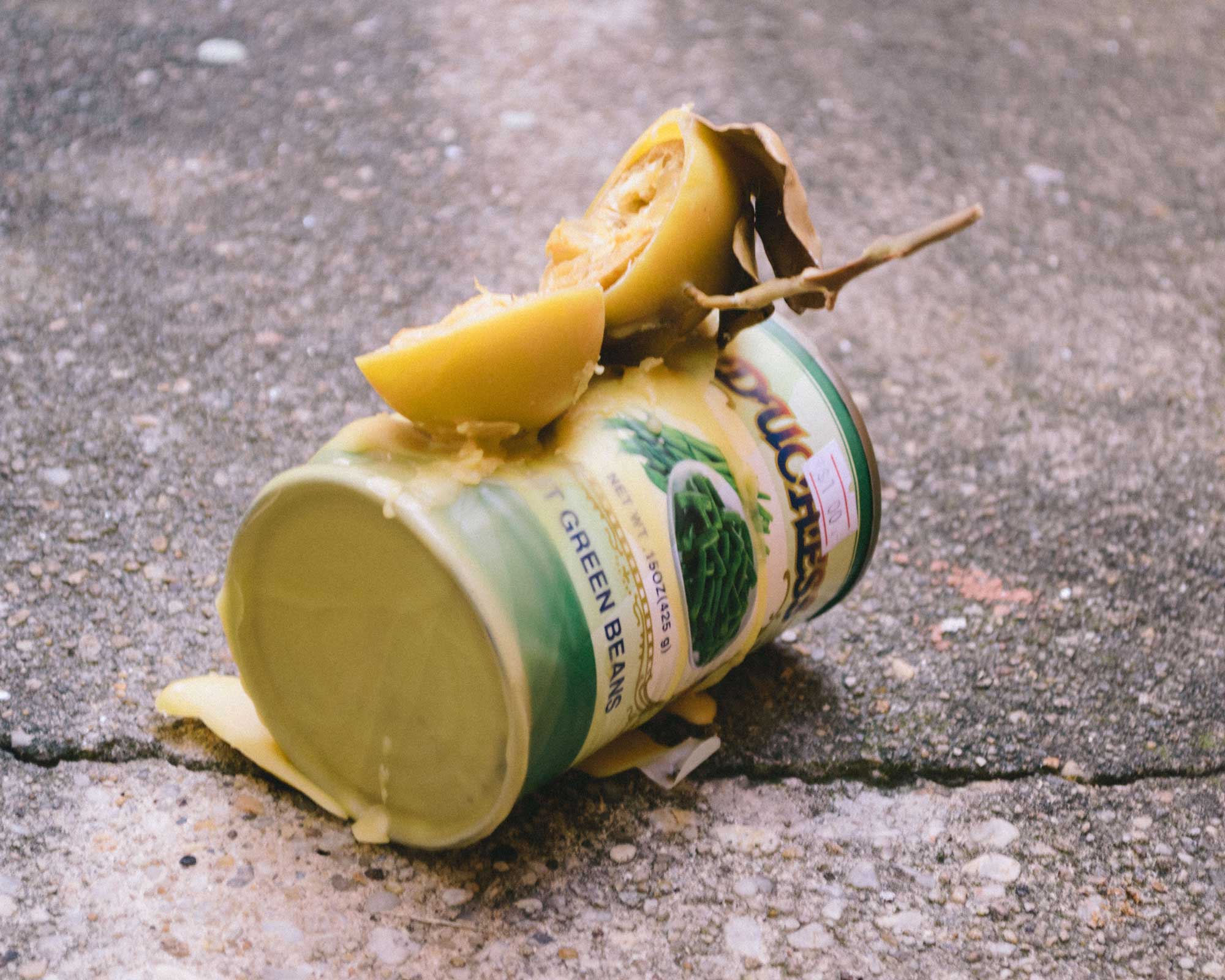 Preserved lemon cut in half sits atop a green aluminum can on its side, the whole of the objects are layered in melted beeswax that has since dried.