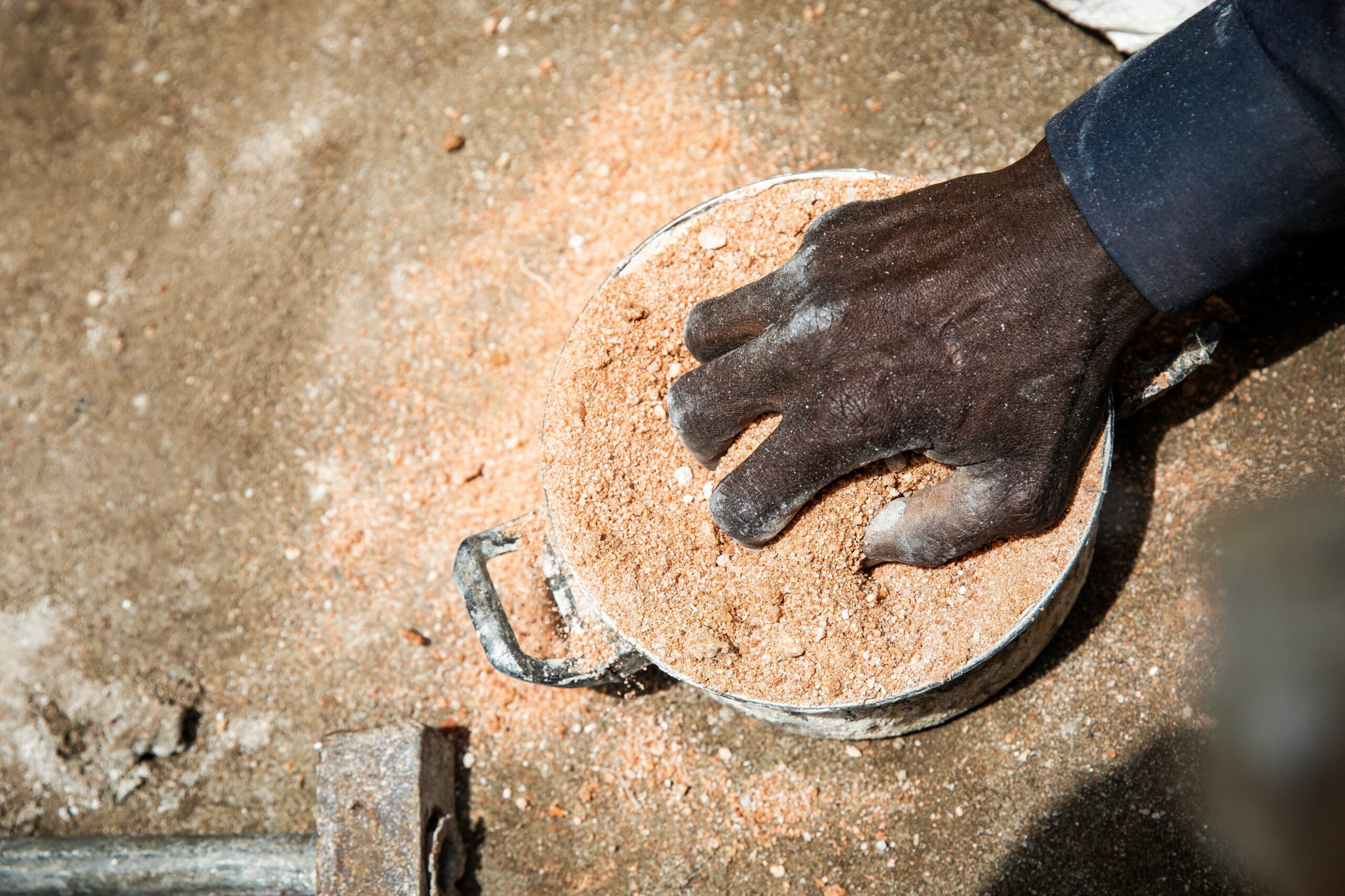 A hand digs into a pot of bronze casting pieces.