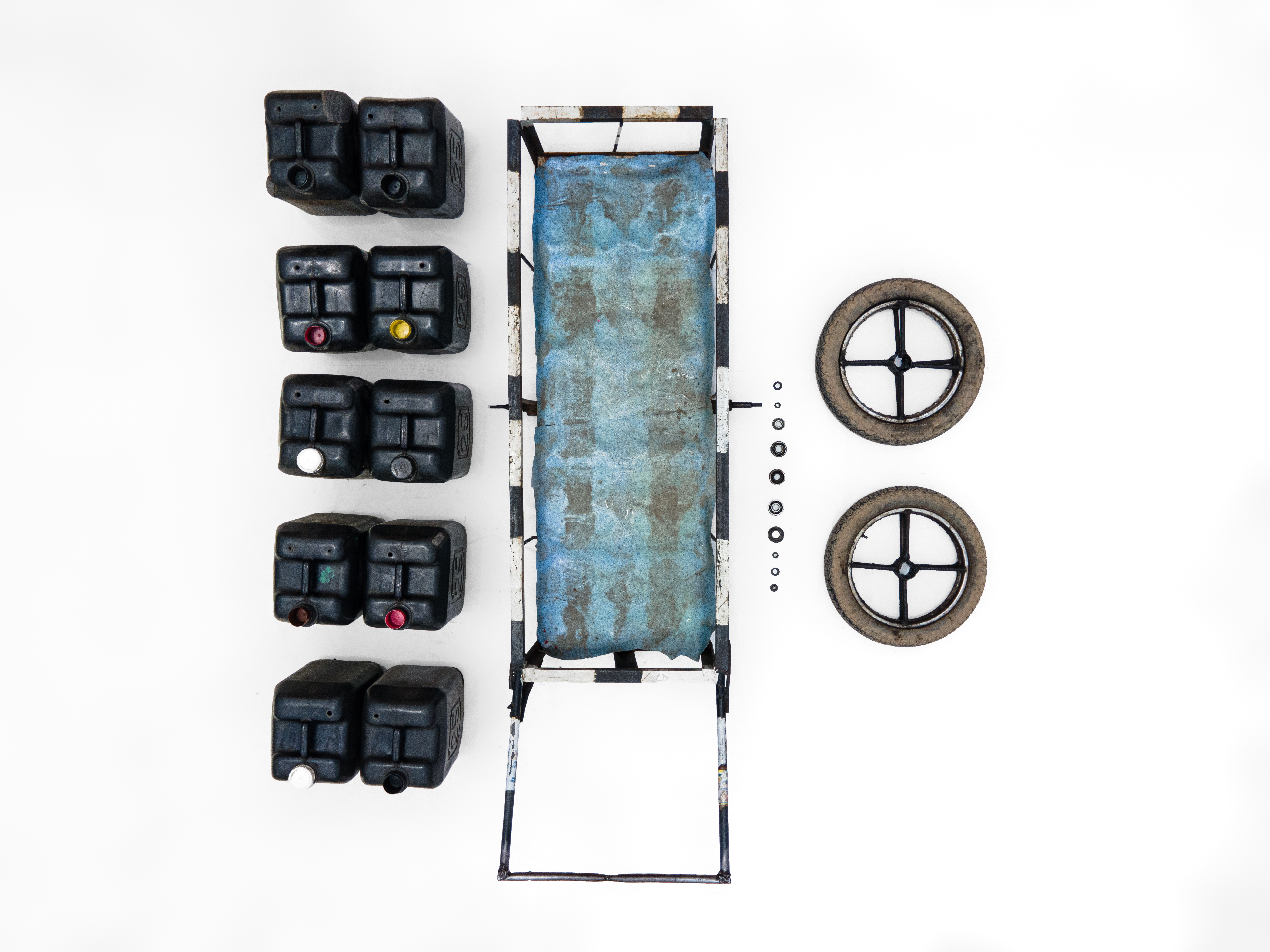 An aerial view of the contents of a meruwa water barrel. Five black jugs of water sit next to the blue trundle. Wheels and screws lay to the side