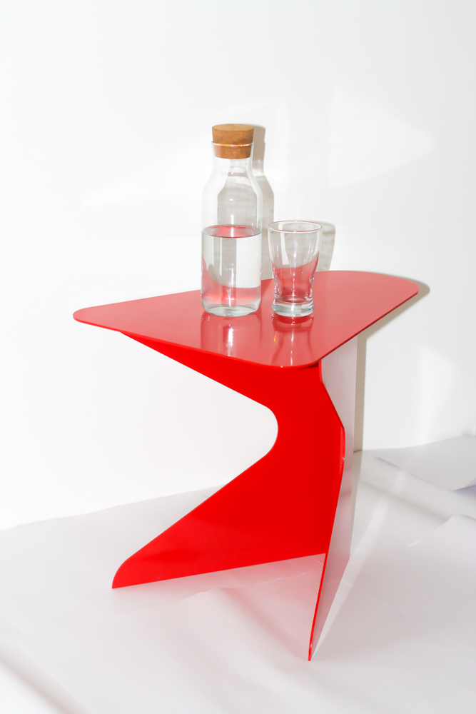 A red bent metal stool sits upright. A carafe of water and empty glass sit atop it.