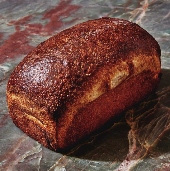 A brown loaf of milk bread sits atop a green and red marbled surface