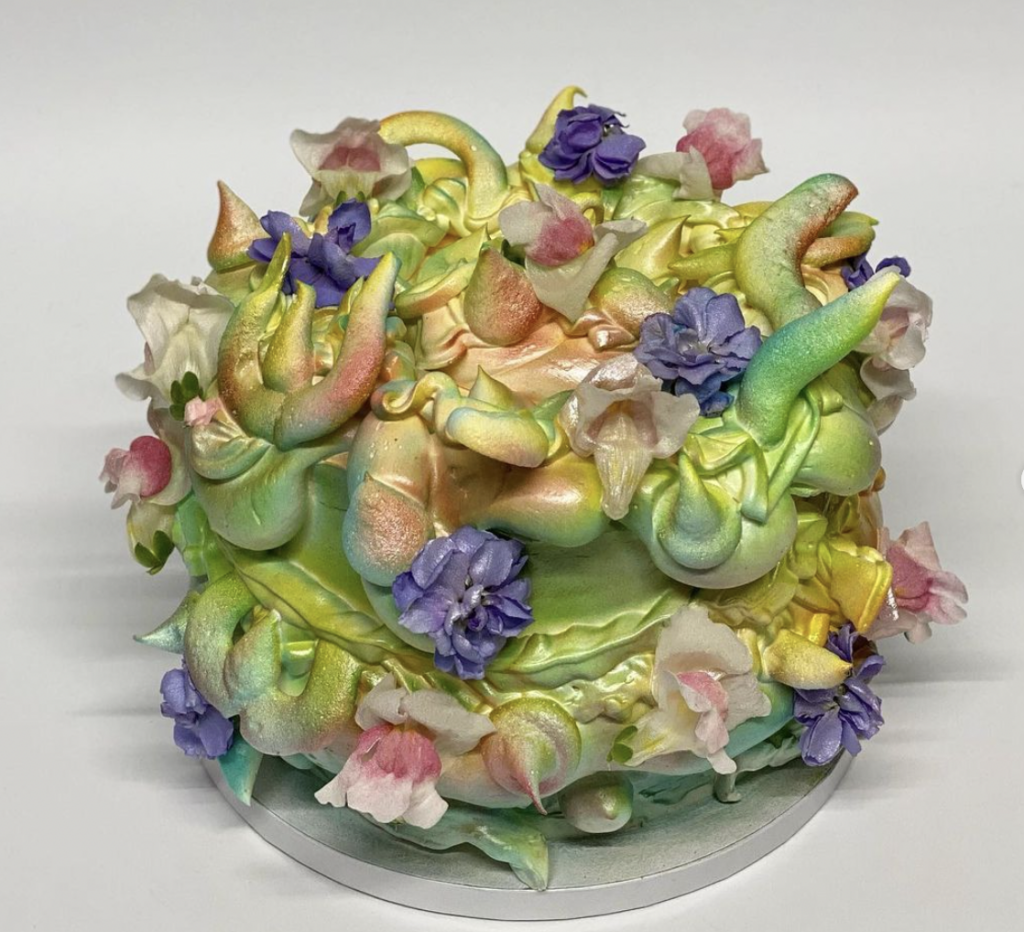 A cake with whorls of frosting protruding. Icing is airbrushed green yellow and pink with purple and pink flowers. 
