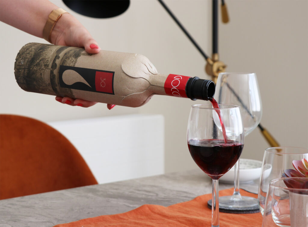 A person pours red wine out of a brown paper bottle into a wine glass. 