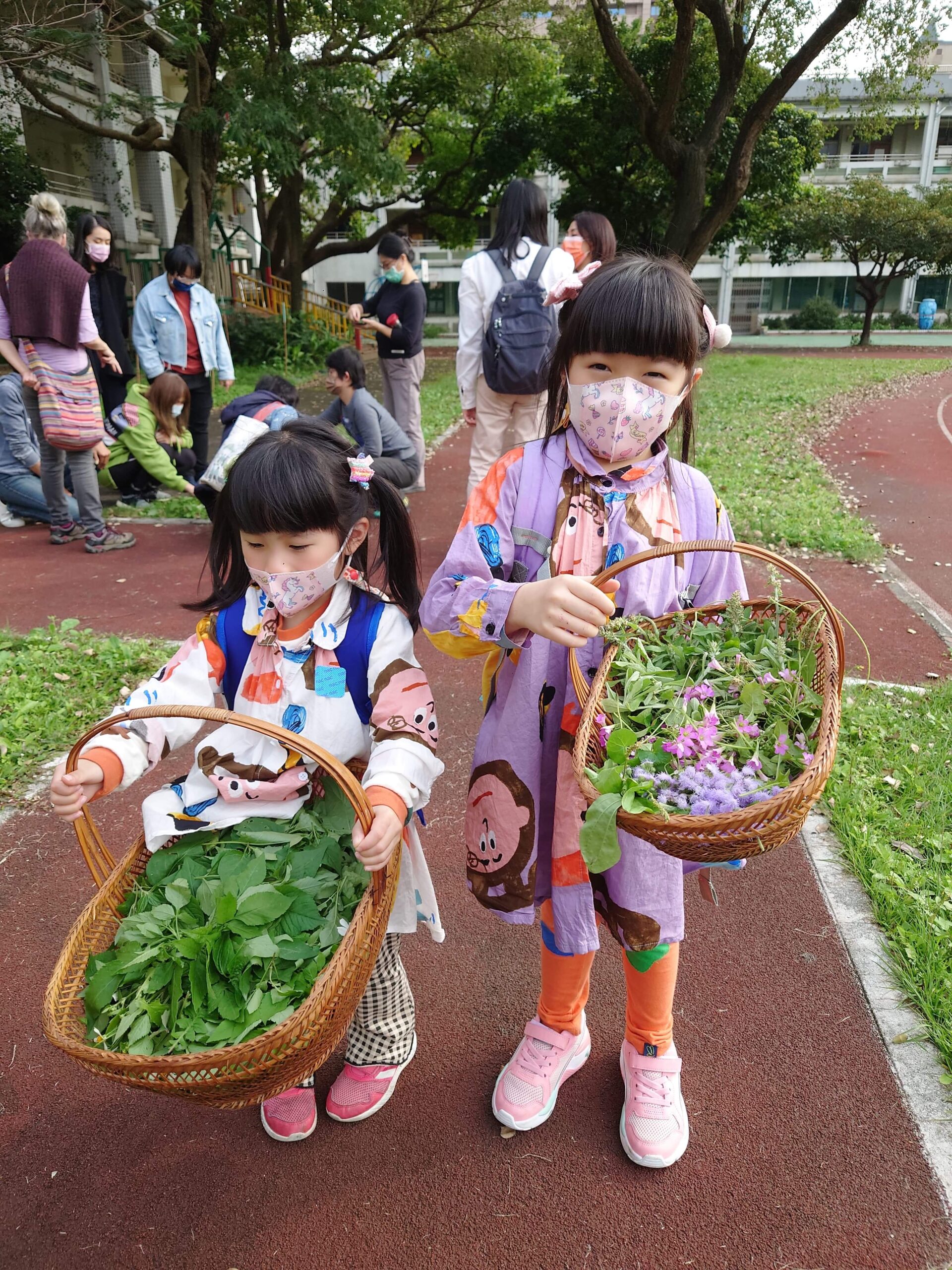 Two small children wearing pigtails hold baskets full of greens they have foraged.