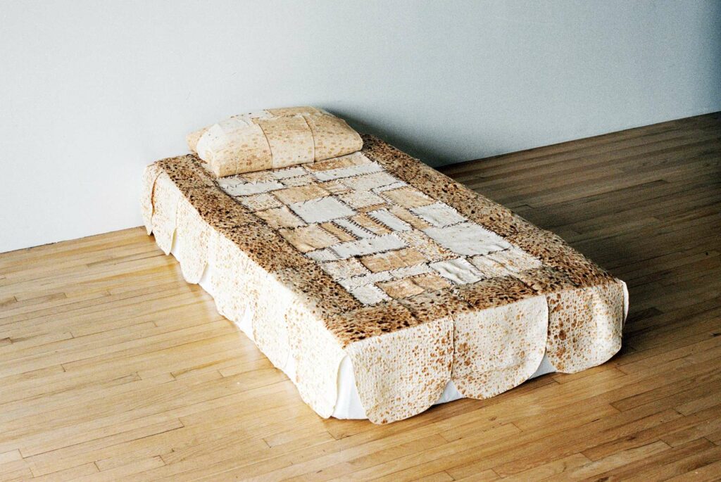 A bed whose duvet cover is created out of stitched lightly browned flatbreads. The pillow is also wrapped in flatbread. 