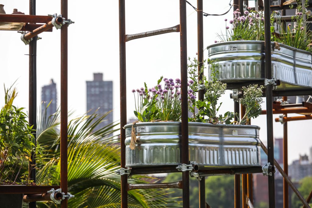 A loose metal scaffolding holds up metal planter tubs filled with flowers, floating in the air.