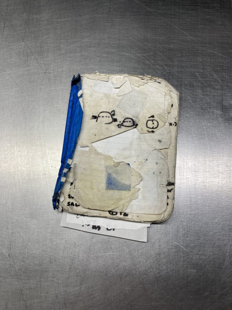A tattered notebook sits on a steel countertop.