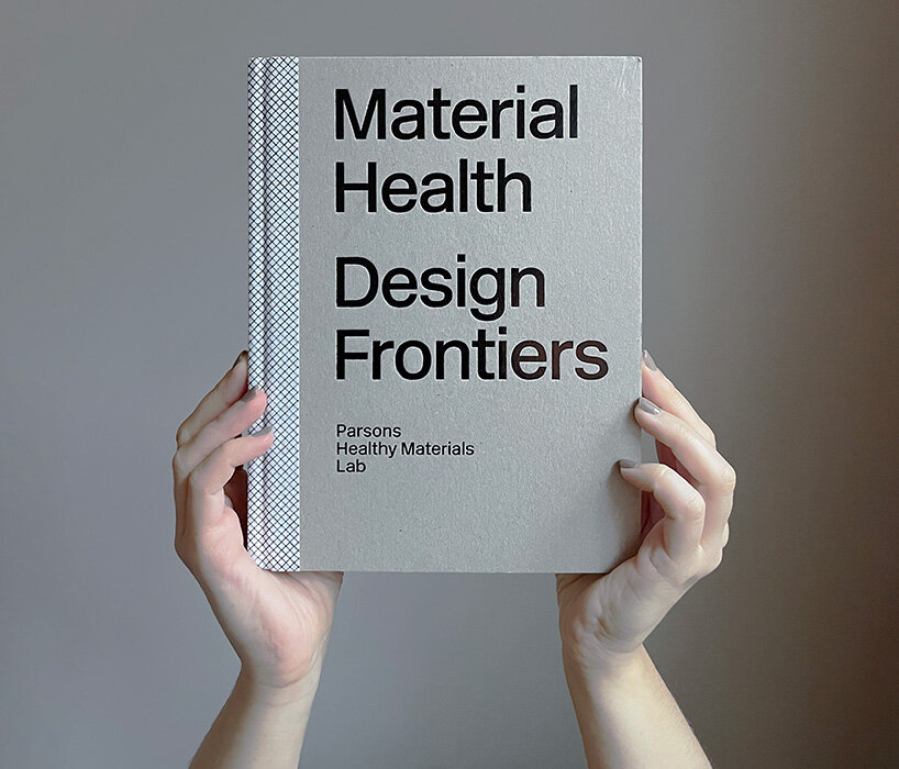 Two hands hold up a beige colored book titled Material Health Design Frontiers.