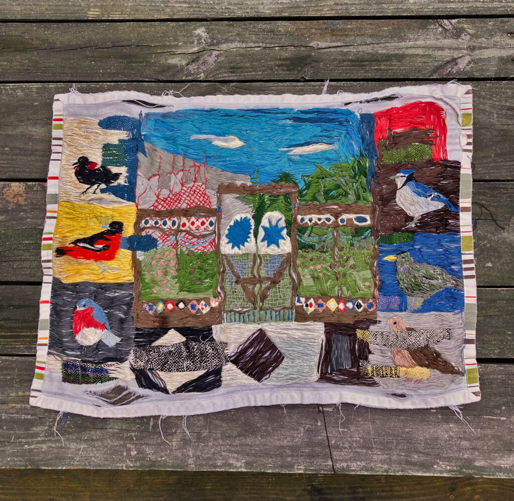 In a small quilt block a variety of birds in various colors are depicted in embroidery.