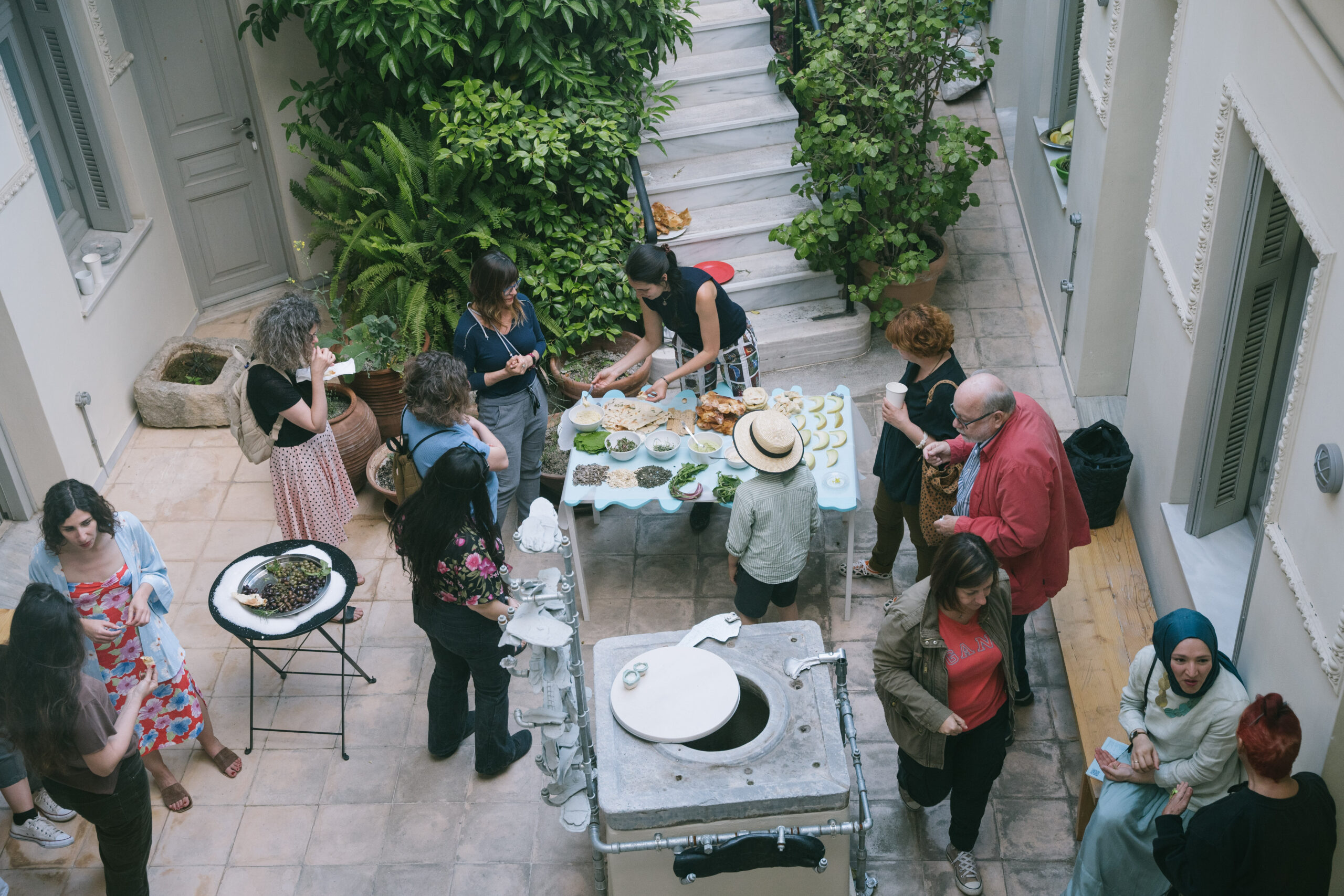 A gathering of people surround a table laden with food in a courtyard.