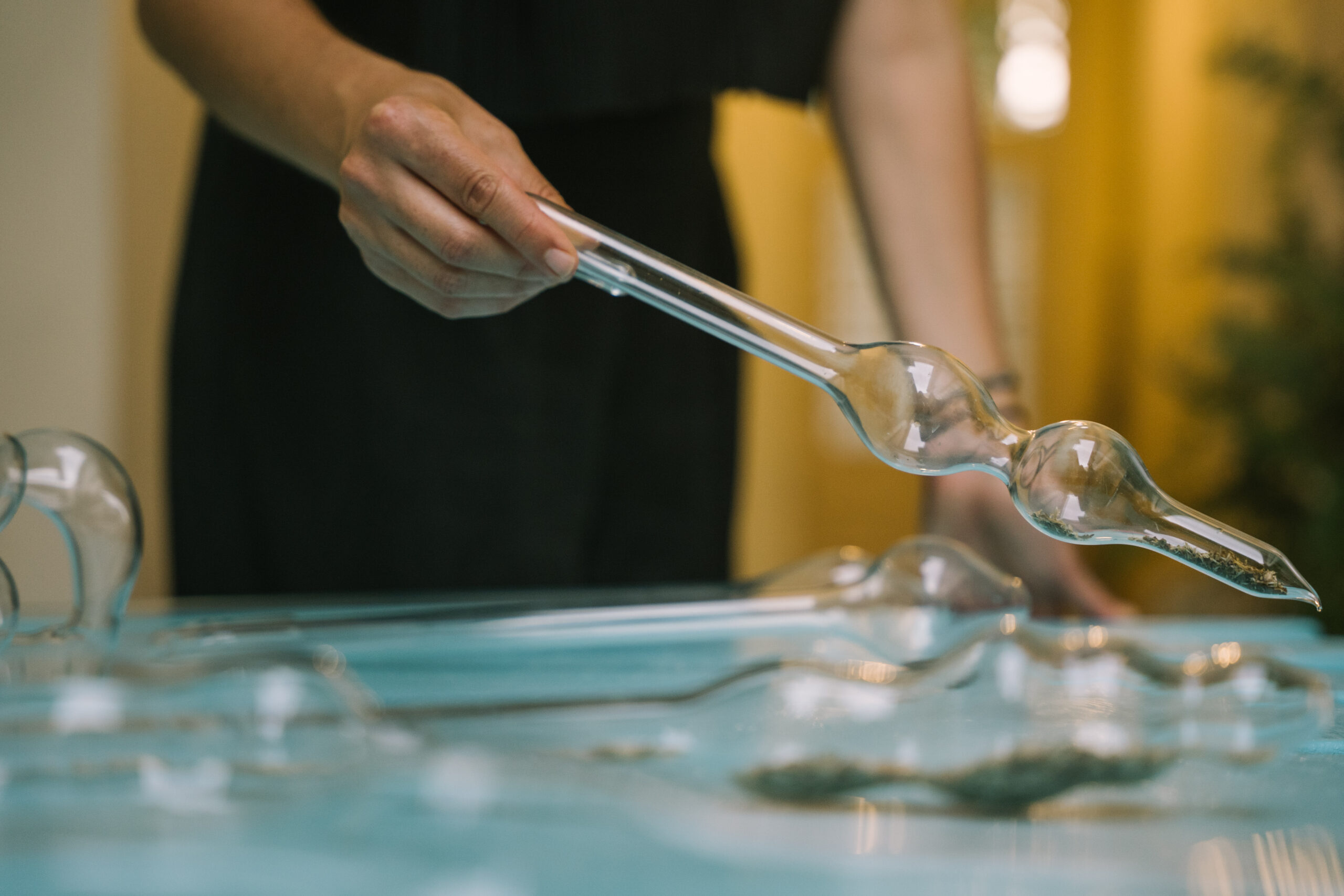 A rounded glass pipette with two bulbs is being used to diffuse scent on a turquoise table.