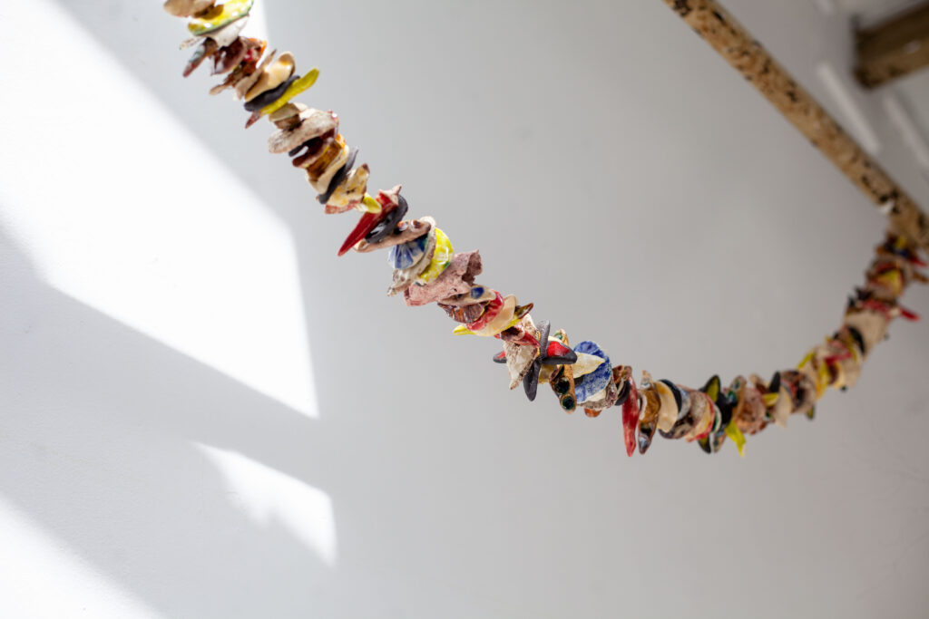 Colorful ceramic shards are hung together into a garland on a string and draped from a beam