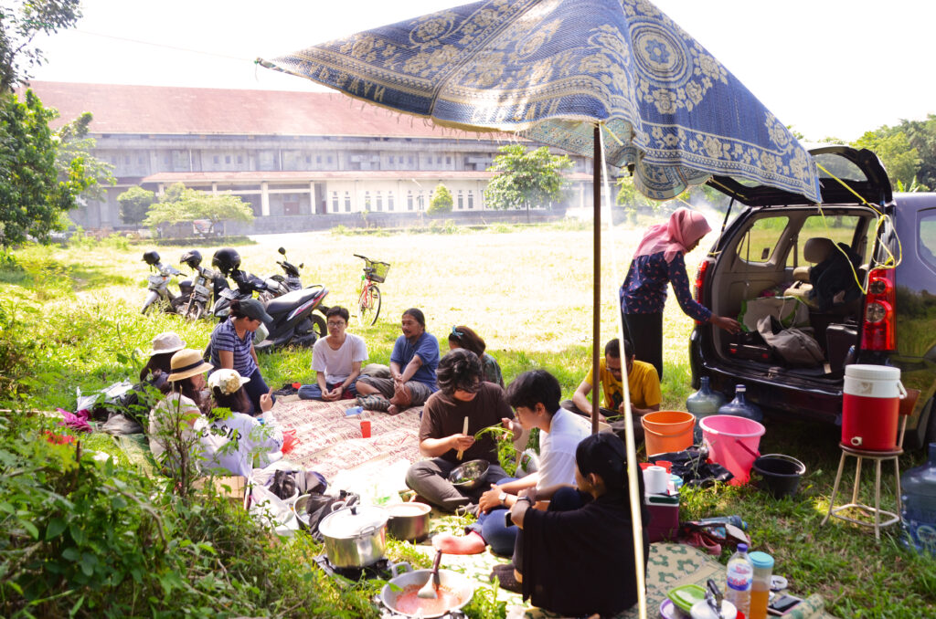 A group of people sit in a field of grass on picnic blankets.