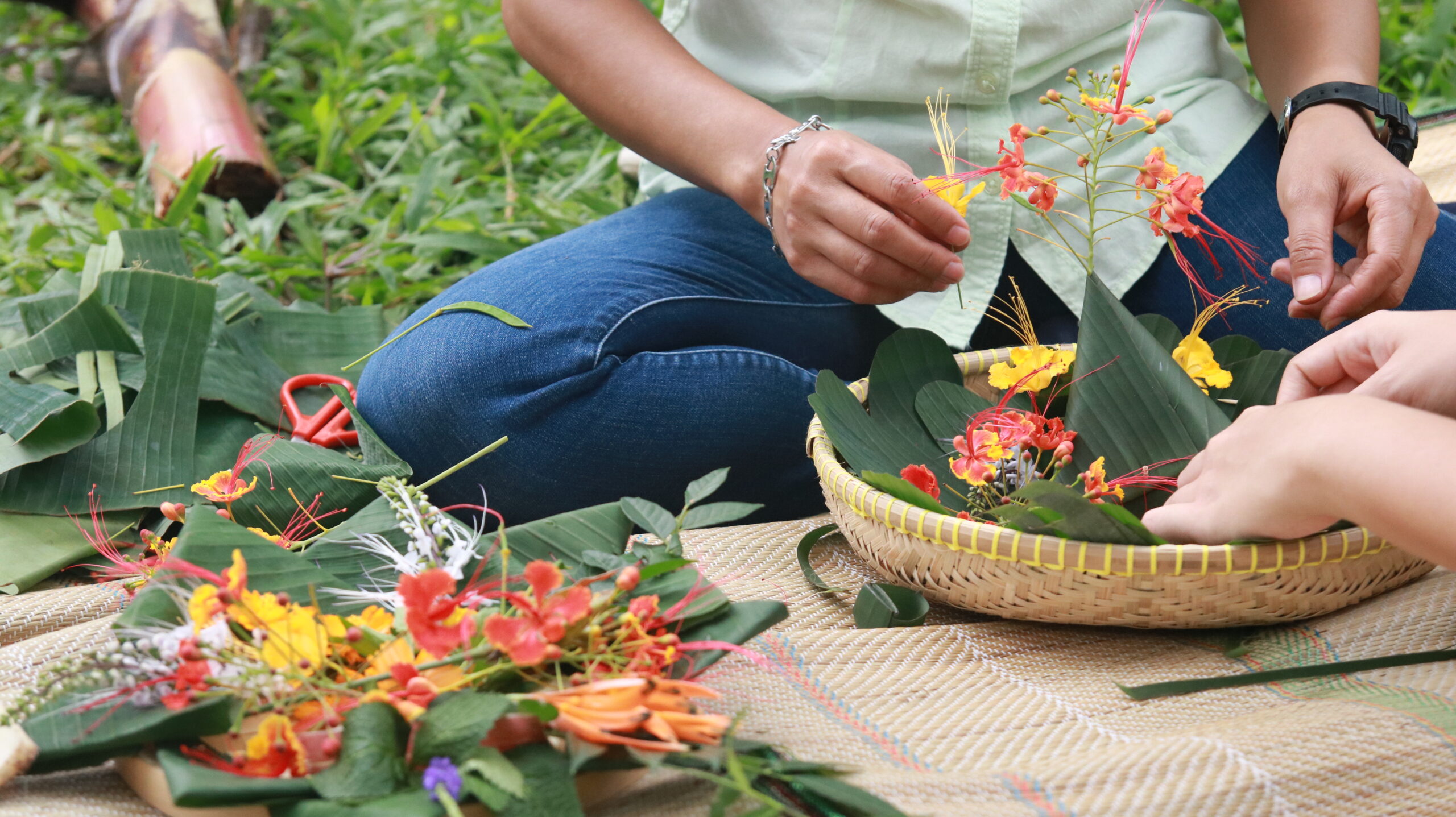 A woman places flowers into a basket of banana leaves.